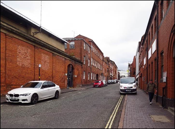 A narrow city street with cars parked on the side of a building

Description automatically generated