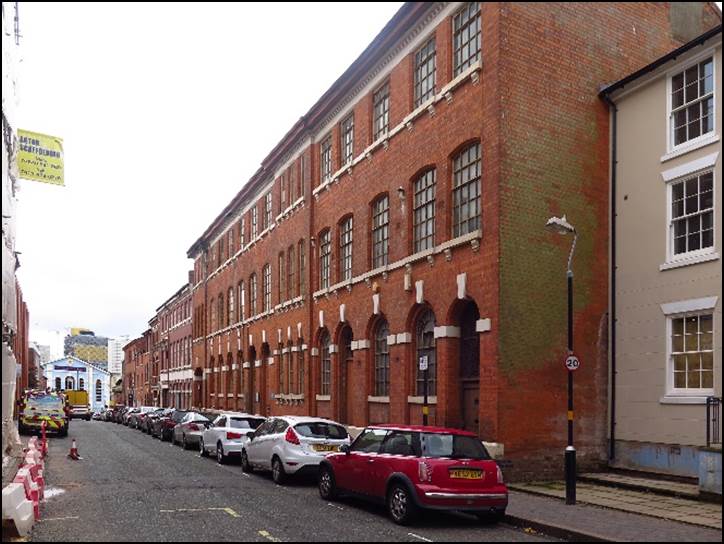 A narrow city street with cars parked on the side of a building

Description automatically generated