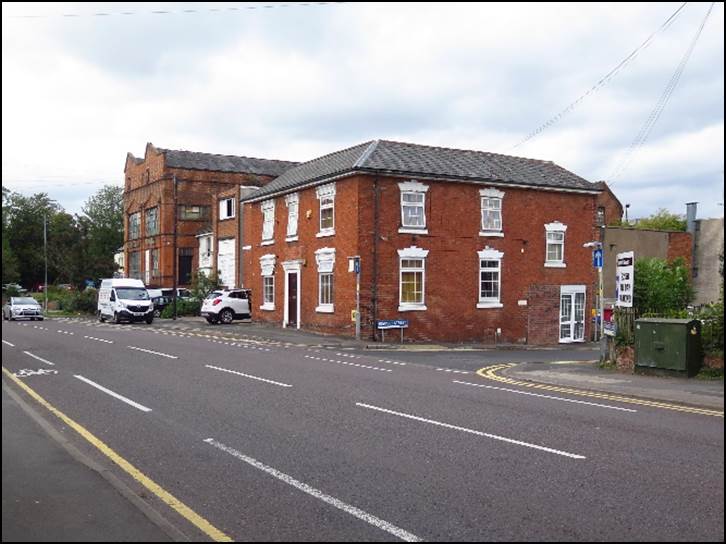 A brick building with cars parked on the side of the road

Description automatically generated with low confidence