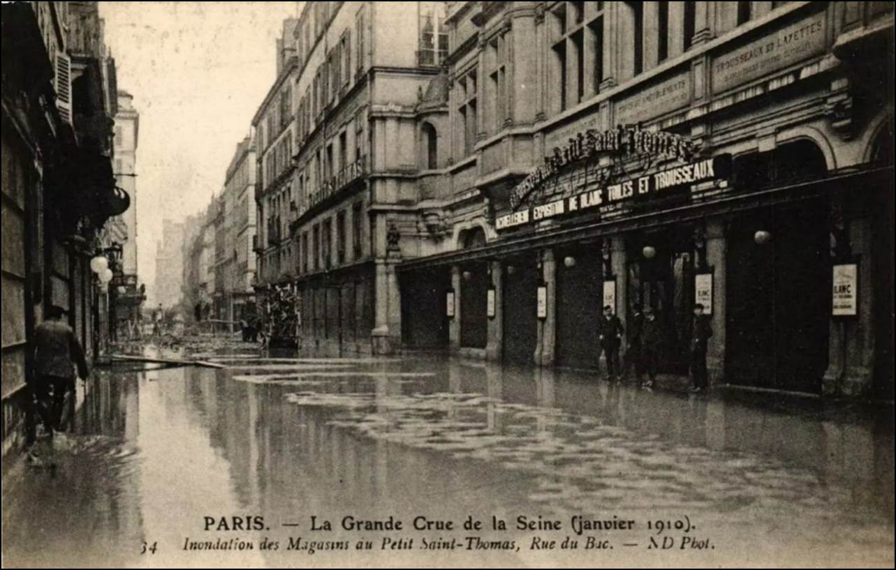 A flooded street with buildings and people walking

Description automatically generated