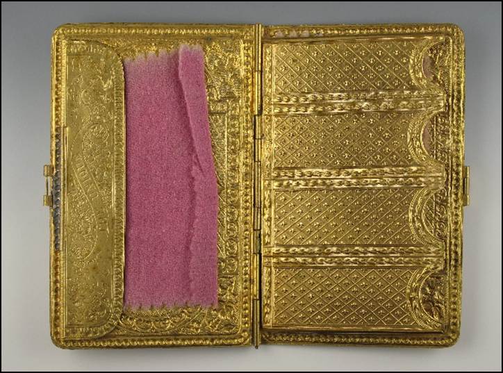 A gold cigarette case with pink fabric inside

Description automatically generated